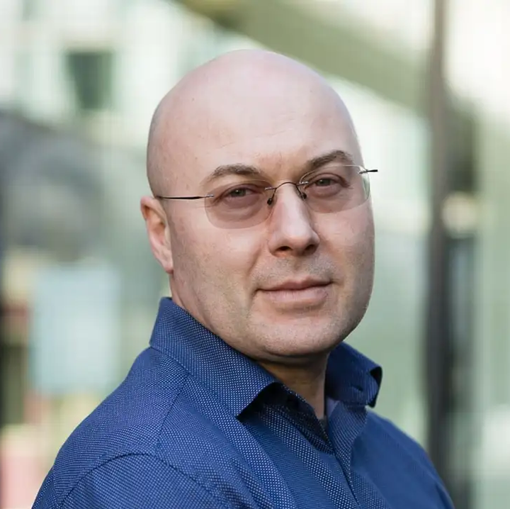 bald man in a blue button-down and tinted glasses
