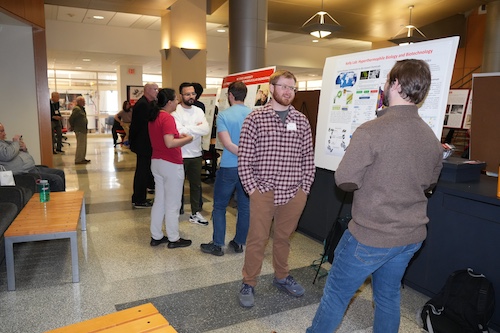 groups of people stand and talk in front of scientific research posters