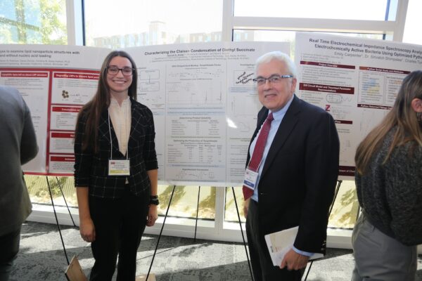 woman and man pose for a picture in front of a research poster